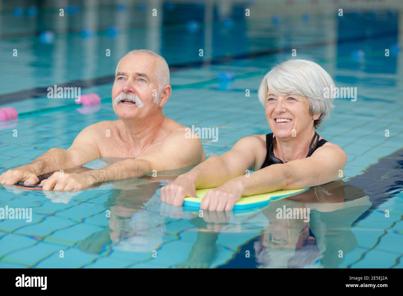 elderly couple following exercise movements in swimming pool Stock