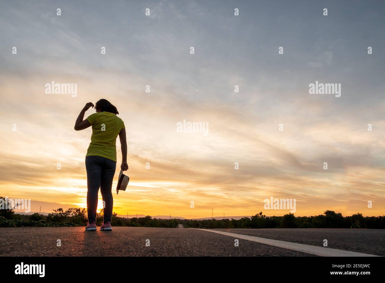 Women wearing t-shirts, jeans, sneakers and hats at sunset, standing along the highway to travel, Happy mood, Vacation concept Stock Photo