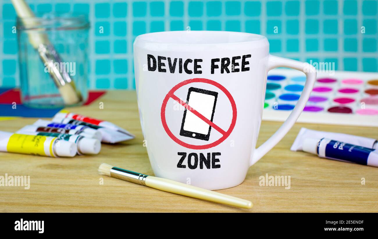 Device Free Zone mug with icon on mug on table surrounded by paints and brushes. Unplug from technology, plug into creativity for good mental health Stock Photo
