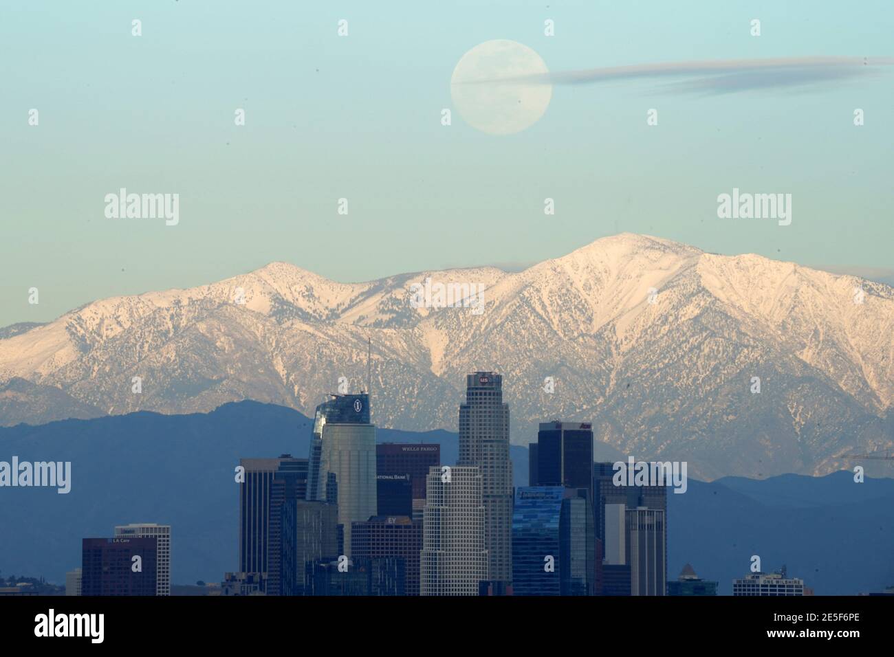 A full moon rises over the downtown Los Angeles skyline with the snow-capped San Gabriel Mountains as a backdrop on Wednesday, Jan. 27, 2021. Stock Photo