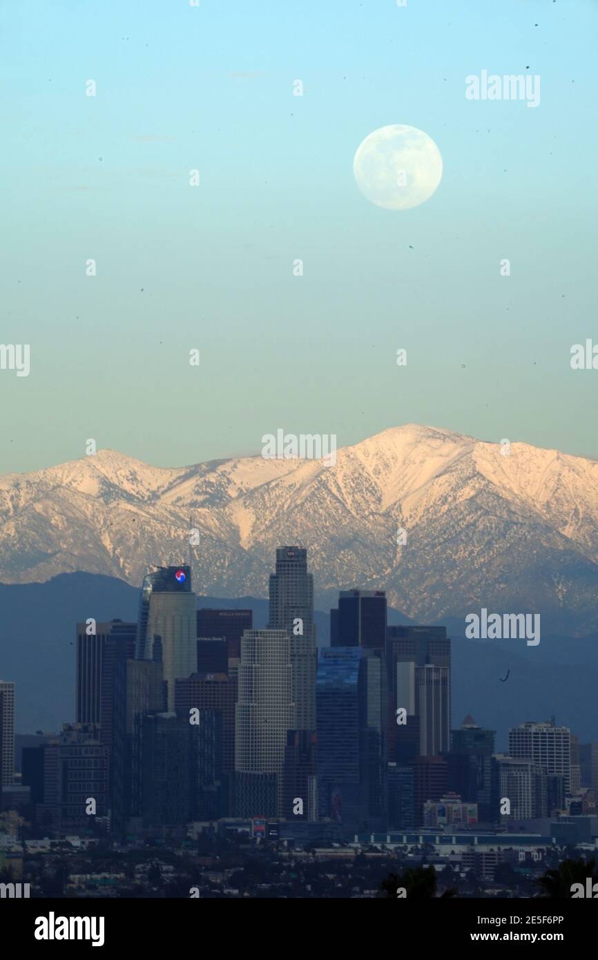 A full moon rises over the downtown Los Angeles skyline with the snow-capped San Gabriel Mountains as a backdrop on Wednesday, Jan. 27, 2021. Stock Photo