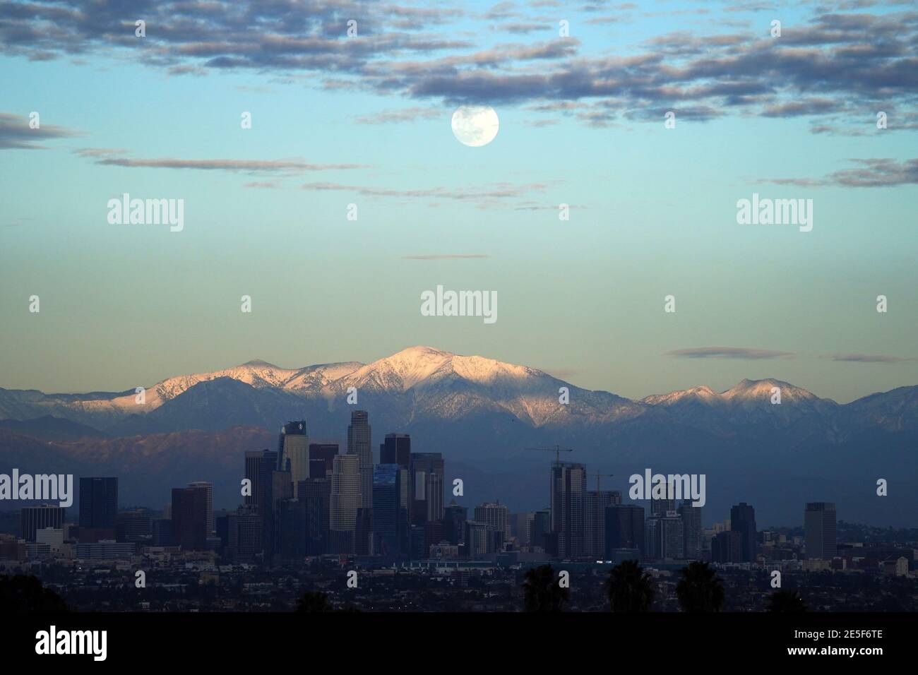 A full moon rises over the downtown Los Angeles skyline with the snow-capped San Gabriel Mountains as a backdrop on Wednesday, Jan. 27, 2021. Stock Photo
