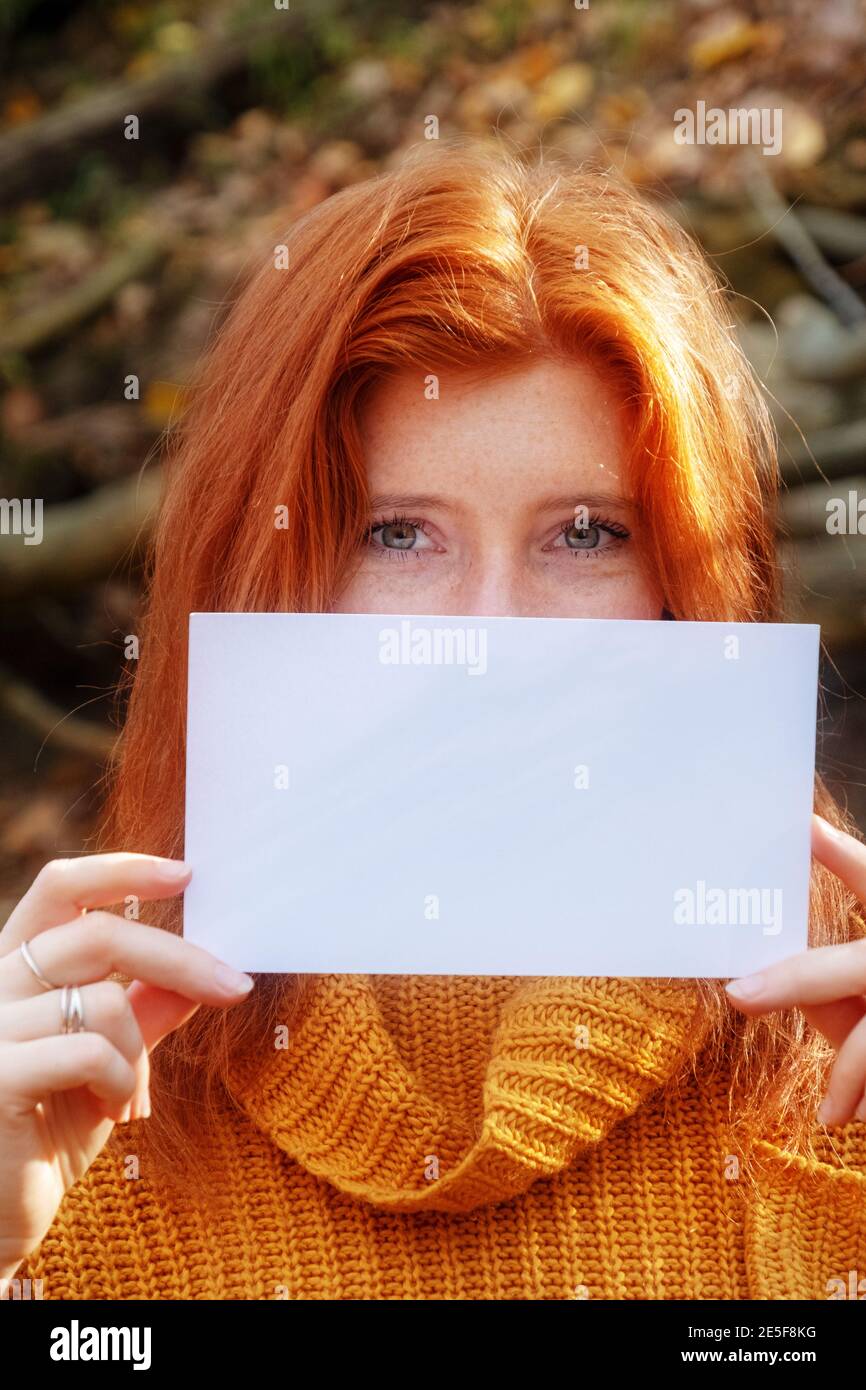 Portrait of beautiful young woman with red hair, ginger smiling holding a blank blank paper in both hands, copy space, place for your text. Stock Photo