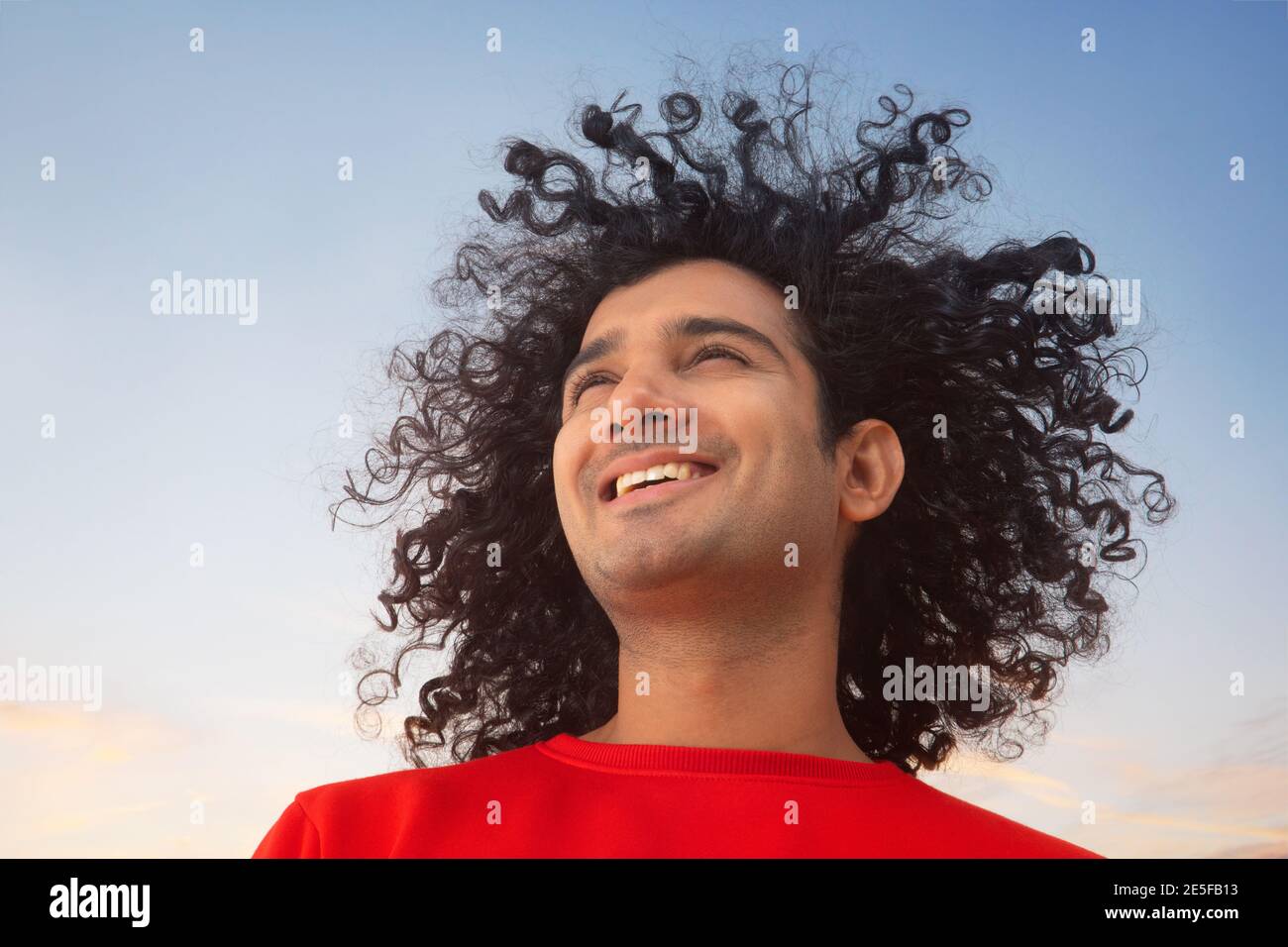 A HAPPY YOUNG MAN WITH CURLY HAIR LOOKING AWAY AND SMILING Stock Photo