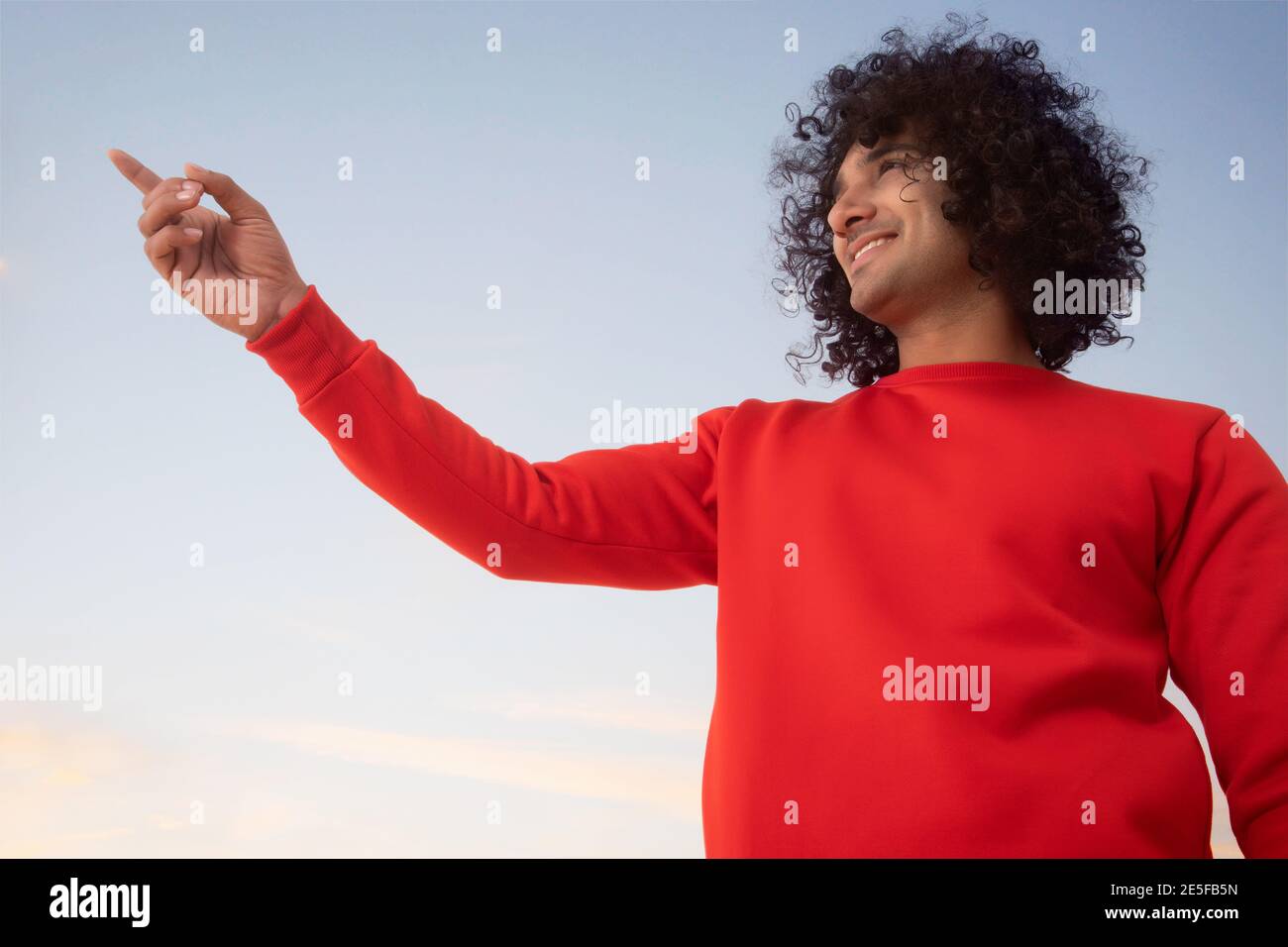 A YOUNG MAN WITH CURLY HAIR STANDING AND HAPPILY POINTING AWAY Stock Photo