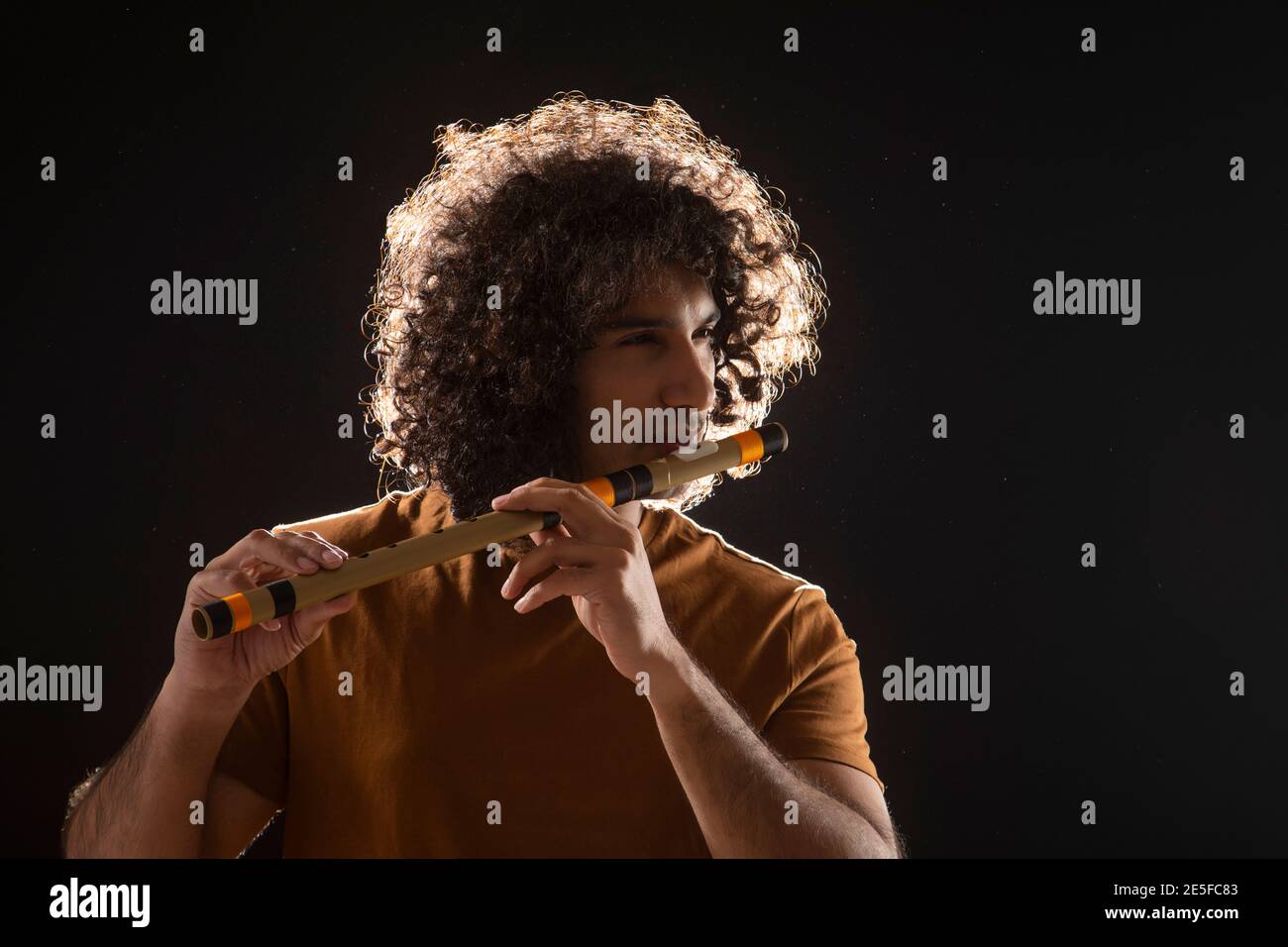 A YOUNG MAN WITH CURLY HAIR STANDING AND PLAYING FLUTE Stock Photo