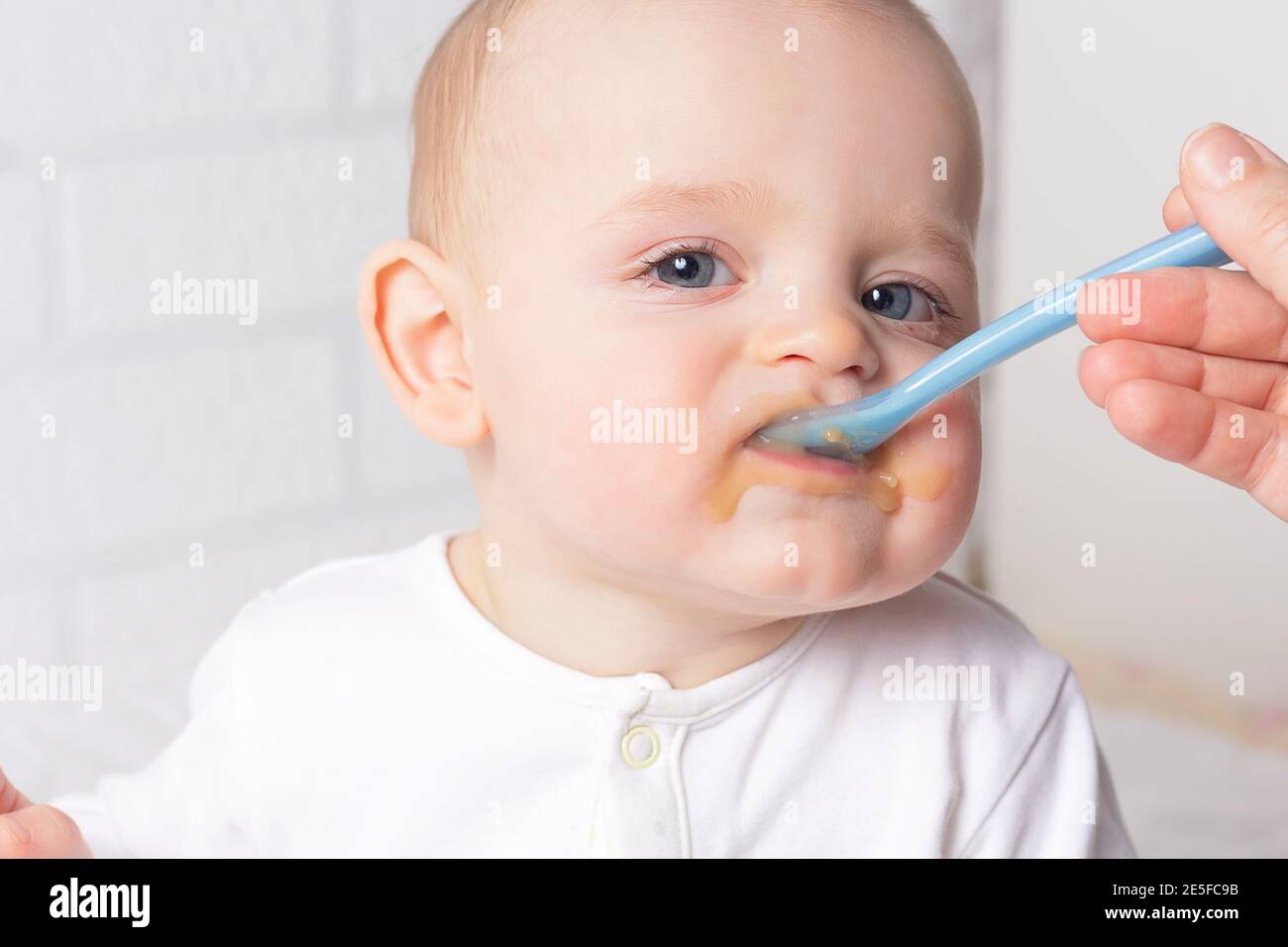 Mother feeding baby with blue baby spoon. First baby fruit puree. Close