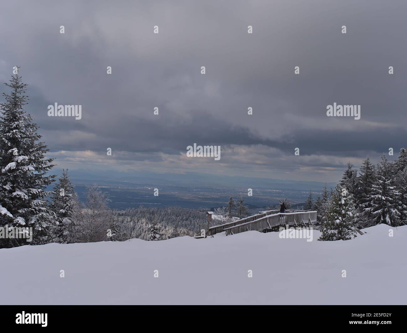 Winter landscape with deep snow and couple enjoying the panoramic view from wooden observation deck near Schliffkopf, Germany in Black Forest. Stock Photo