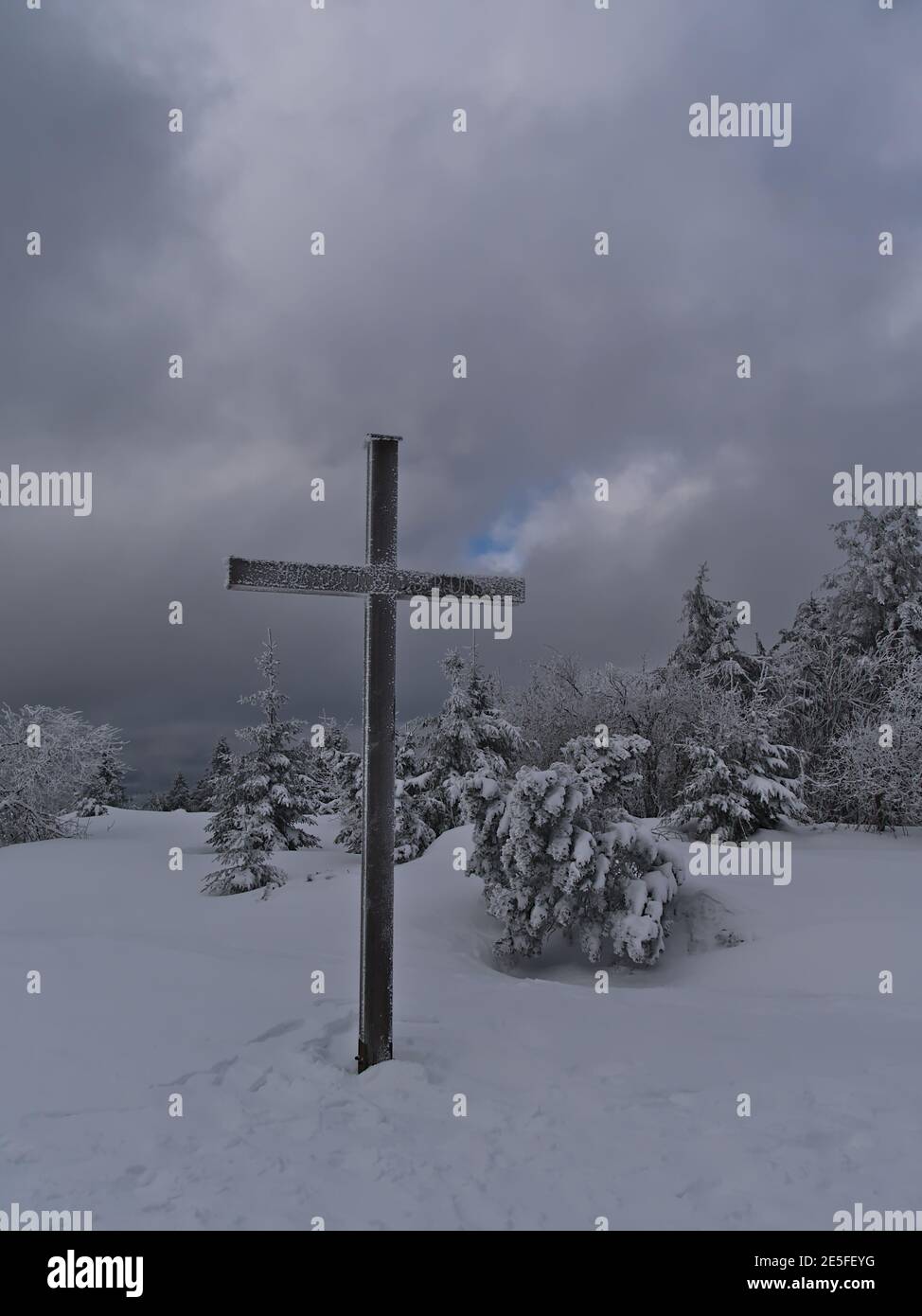 Wooden religious cross on the top of Schliffkopf peak in the Black Forest hills, Germany in deep snow with frozen coniferous trees on cloudy day. Stock Photo