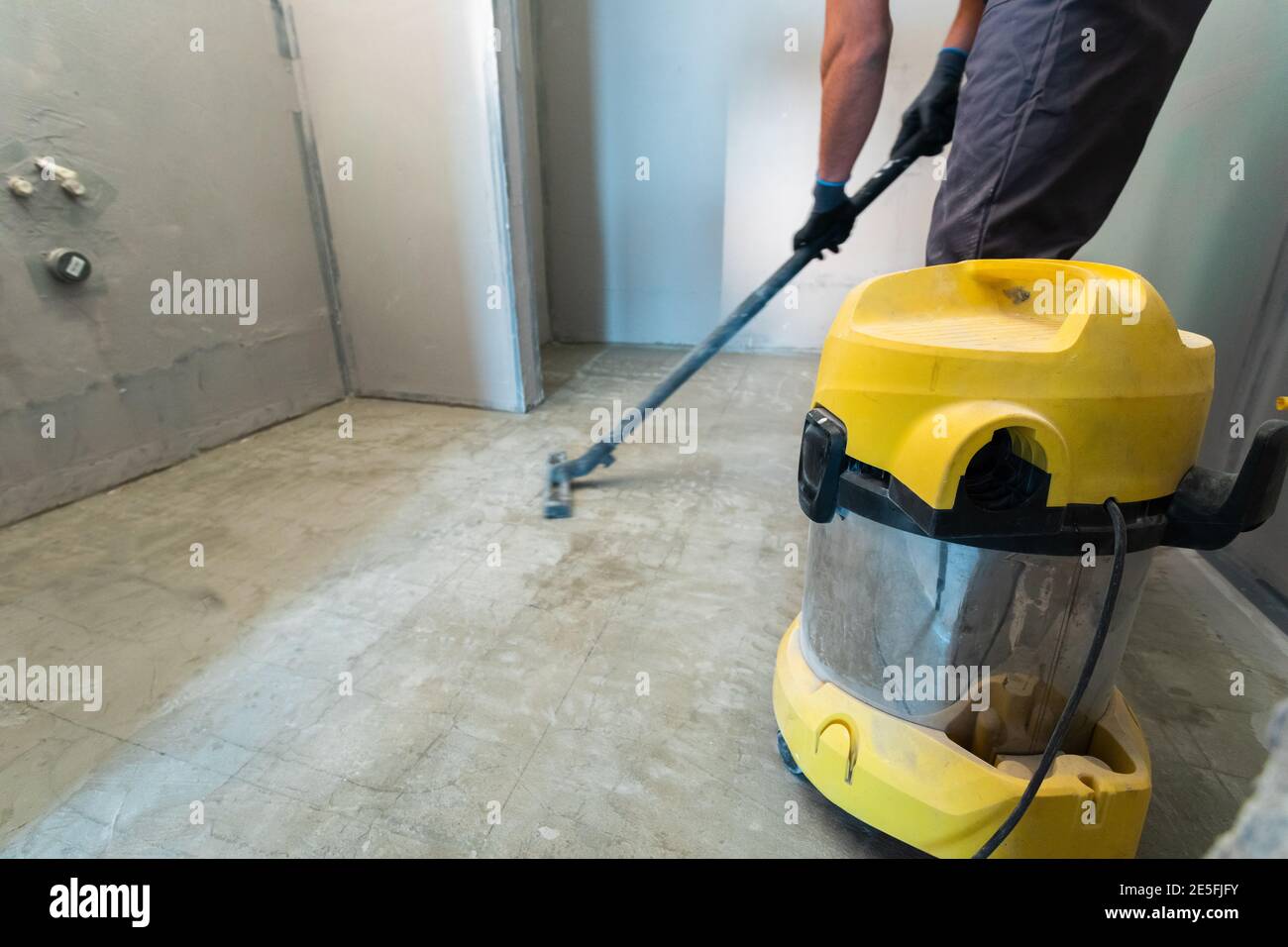 The builder cleans the floor from dust with a construction vacuum