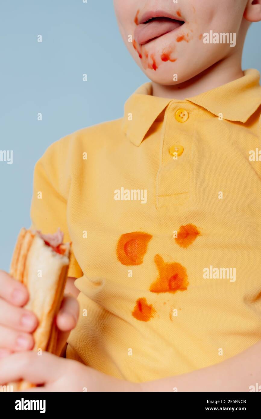 dirty ketchup Sauce stains on a yellow child t-shirt. child licking the sauce on his face Stock Photo