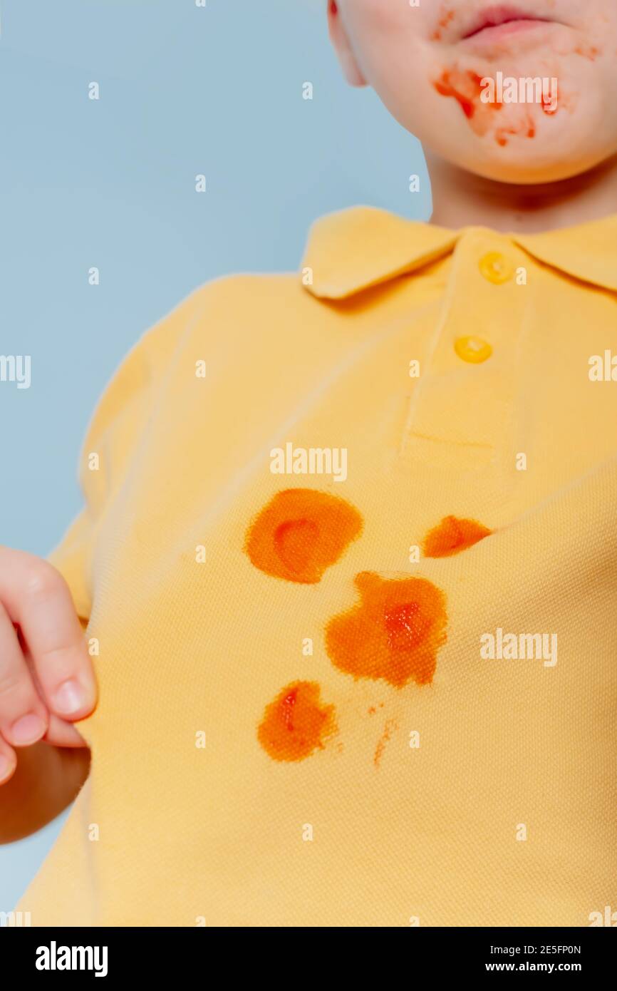 dirty ketchup Sauce stains on a yellow child t-shirt. Child ruining her t-shirt with tomato sauce eating Hot Dog. Stock Photo
