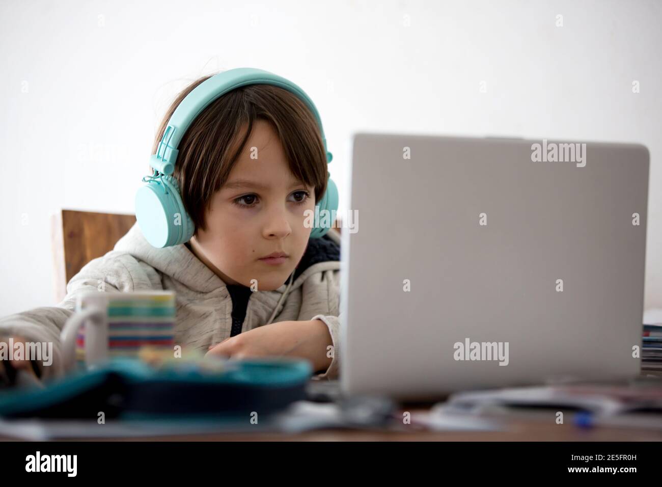 School child, sitting at the table with laptop, writing school tasks ...