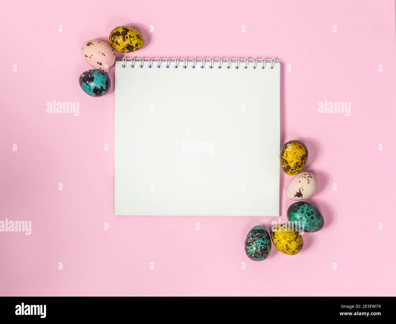 a blank sheet of paper surrounded by easter eggs on a pink background Stock Photo