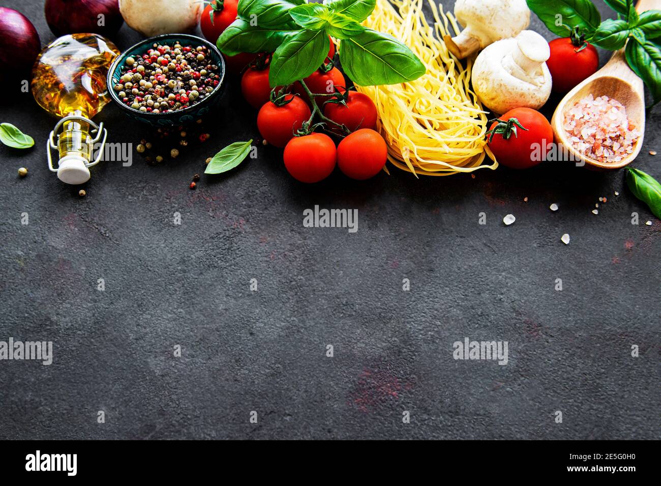 Healthy mediterranean diet, ingredients for Italian meal, spaghetti, tomatoes, basil, olive oil, garlic, peppers on black background Stock Photo