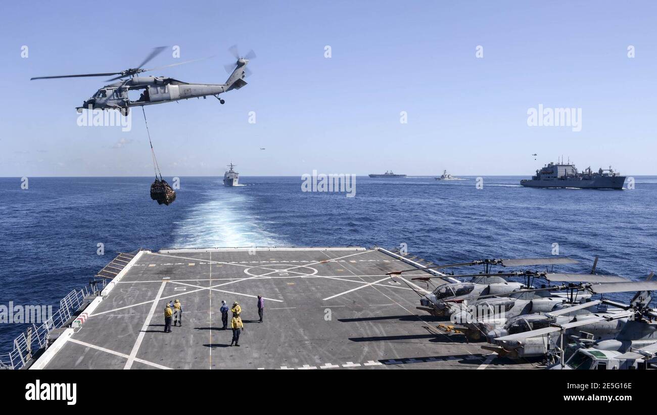 MH-60 Seahawk helihoisting cargo off flight deck of USS Green Bay (LPD-20) with USS Ashland (LSD-48), USS Bonhomme Richard (LHD-6), USS Preble (DDG-88), and USNS Amelia Earhart (T-AKE-6) in background 150705 Stock Photo