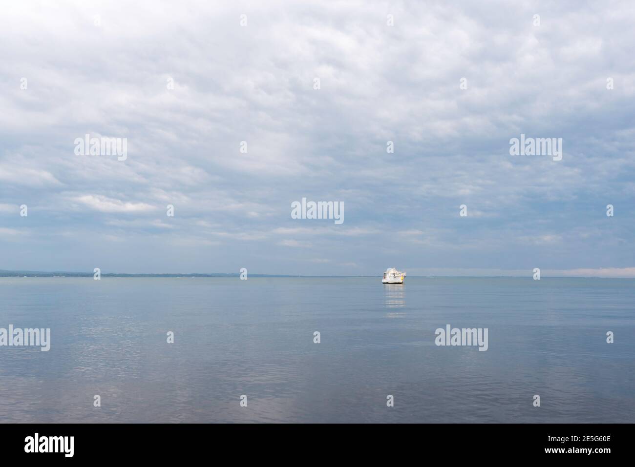 A lone white motor cruiser boat sits on glassy water in Port Stephens reflecting grey rain clouds above Stock Photo