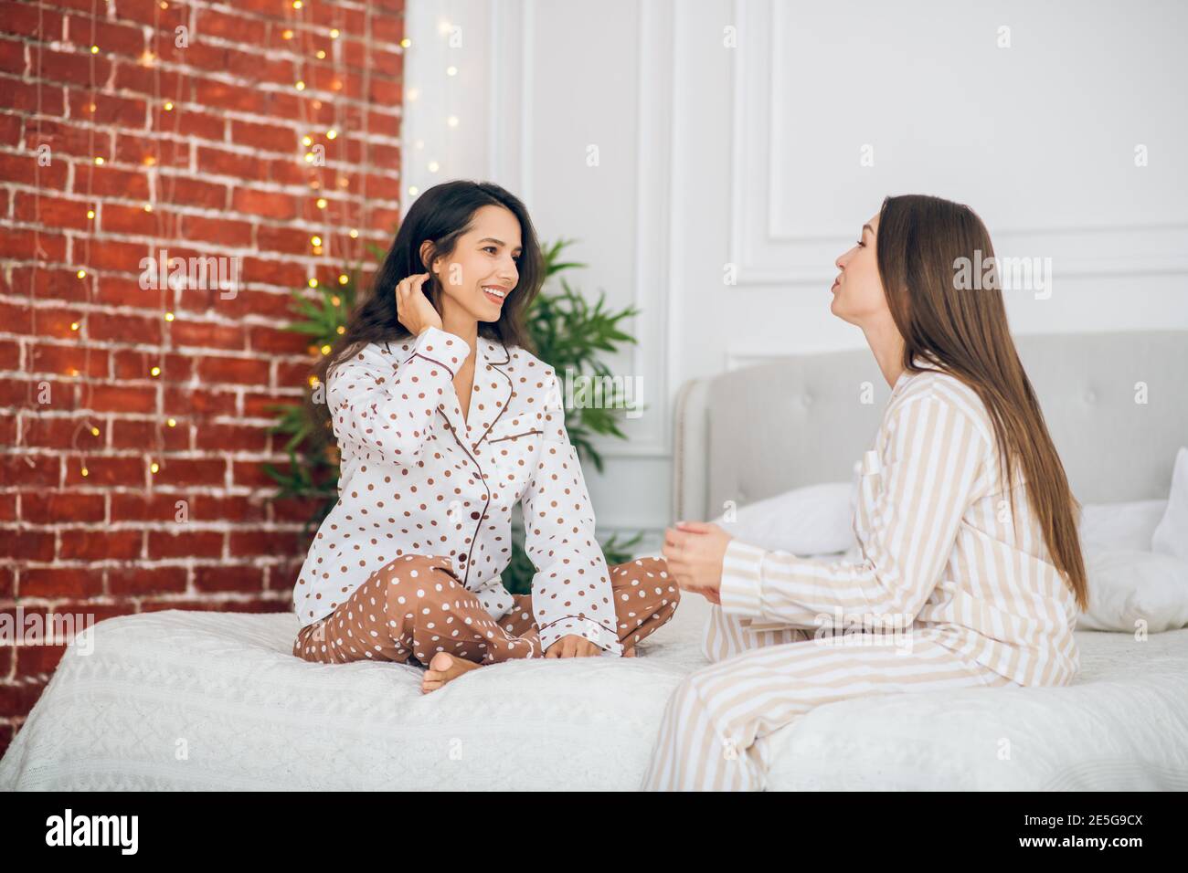 Two young girls in pajamas sitting on a bed and talking Stock Photo