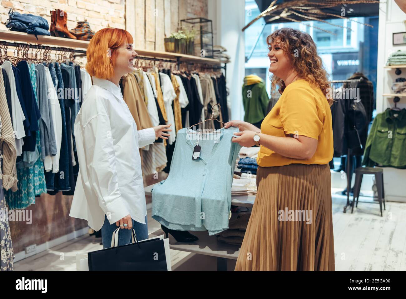 Fashion store owner holding a top and showing it to a female customer. Woman working in a fashion shop assisting shopper. Stock Photo