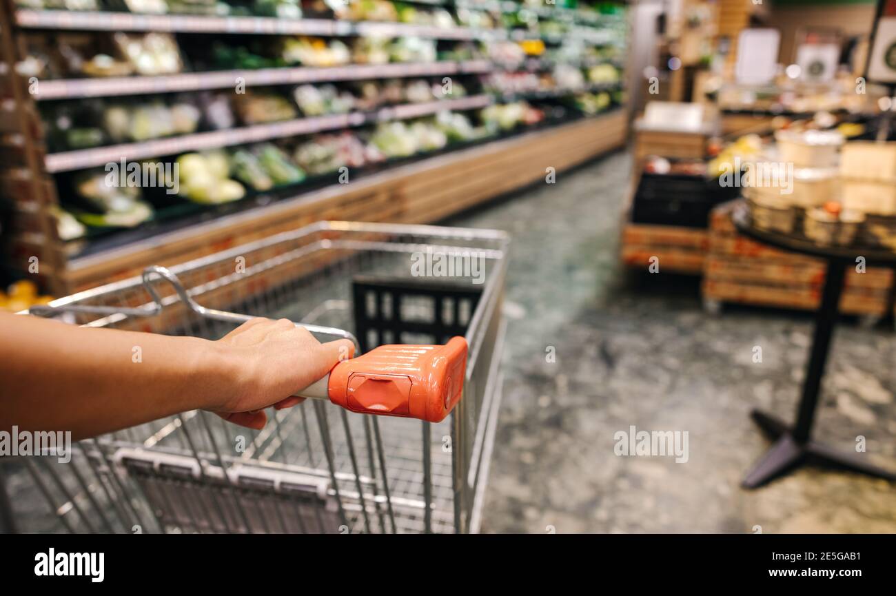Closeup of a customer hands pushing shopping cart in grocery store. Shopper with cart in supermarket. Stock Photo