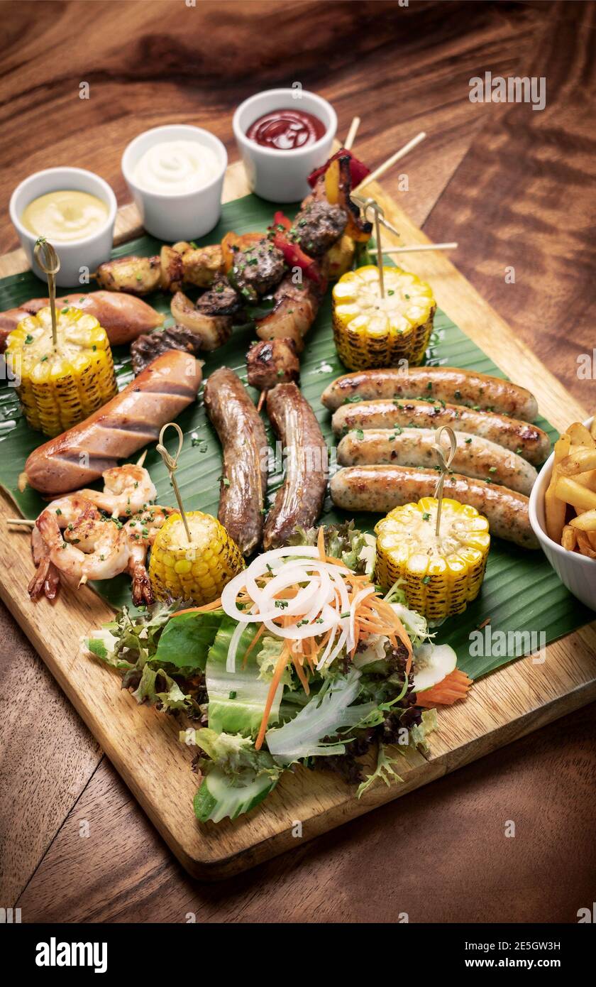 organic mixed grill barbecue meat platter rustic set meal with sausages, skewers, side dishes and sauces Stock Photo