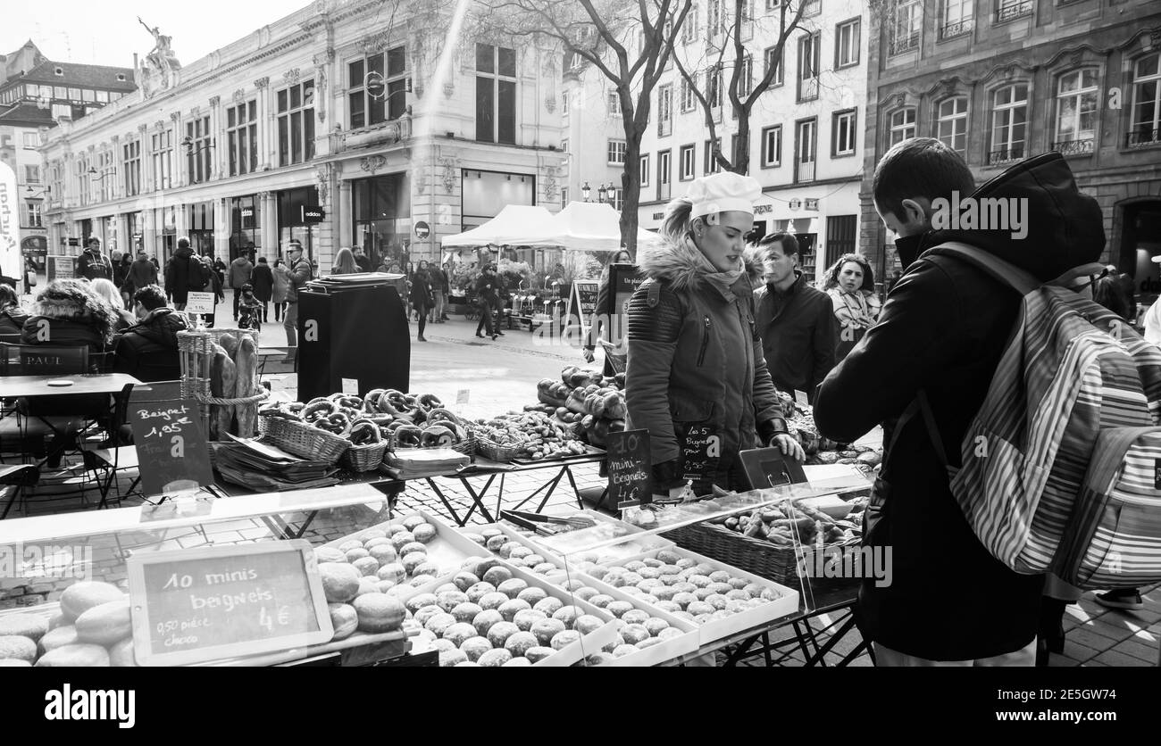 Strasbourg, France - Feb 23, 2018: People pedestrians buying at the outdoor market stall bagels french croissants and other bakeries from Paul pastries store boulangeries - black and white image Stock Photo