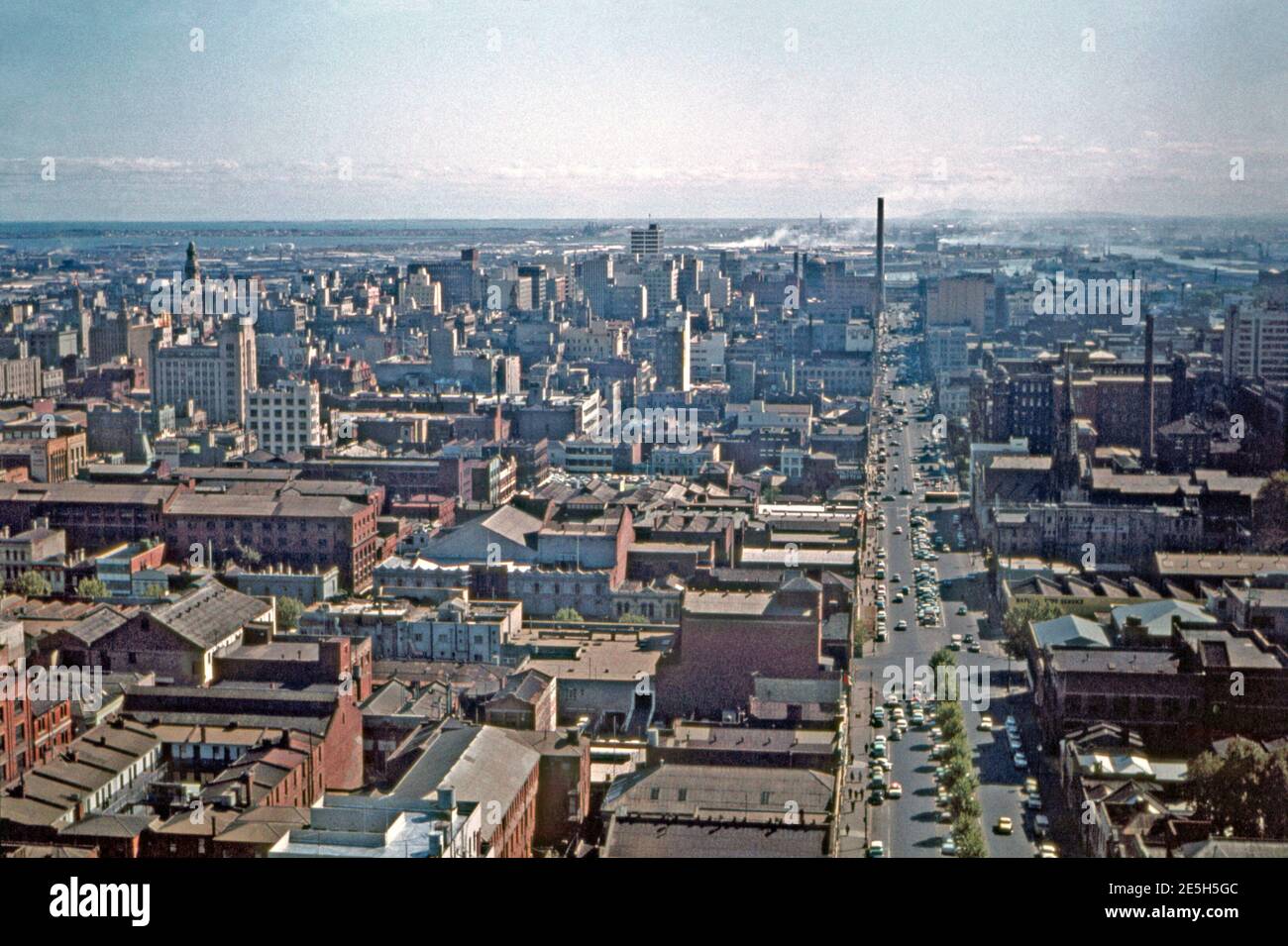 An aerial view looking west over Melbourne, Victoria, Australia in 1961, in the city’s central business district. The wide street is Lonsdale Street. Manufacturing and factory activity visible in the 1960s has almost completely been replaced by far taller buildings with a mixture of retail, office, hotel and residential usage. In the background is the Yarra River and the port district of the city. Stock Photo