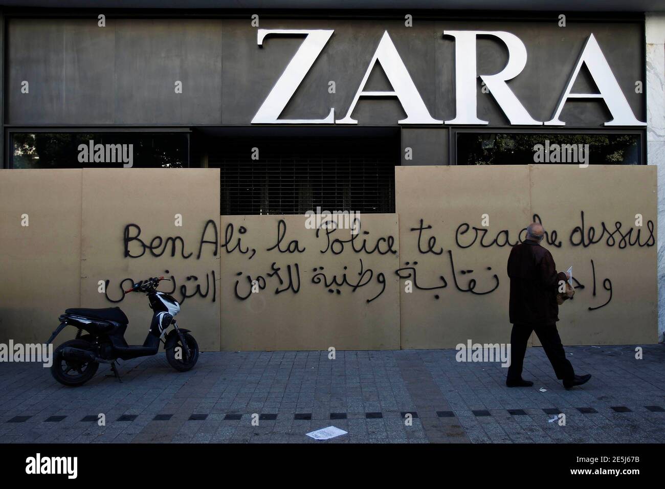 A man walks past a boarded up Zara shop with graffiti denouncing ousted  president Zine al-Abidine Ben Ali, in downtown Tunis, January 23, 2011.  Protesters from Tunisia's poor rural heartlands demonstrated in