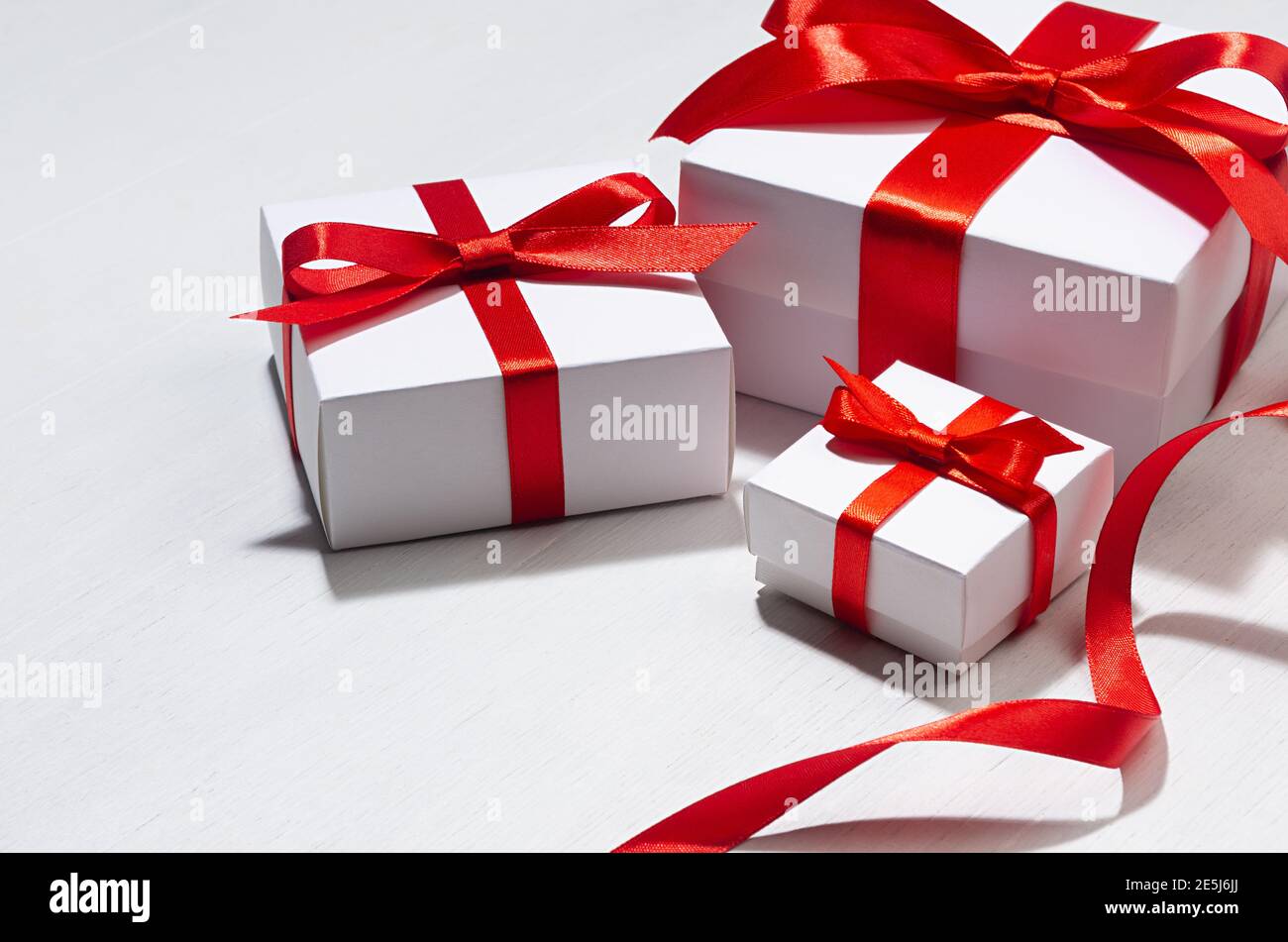 White different size gift boxes with red silk ribbon on white wood