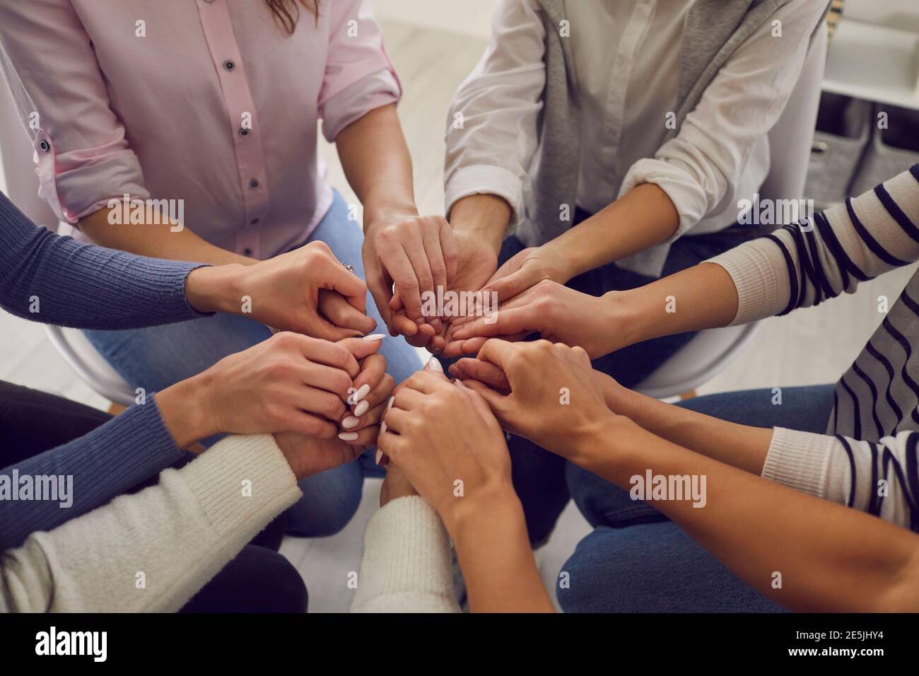 Group of women sitting together and holding hands, demonstrating support and solidarity Stock Photo