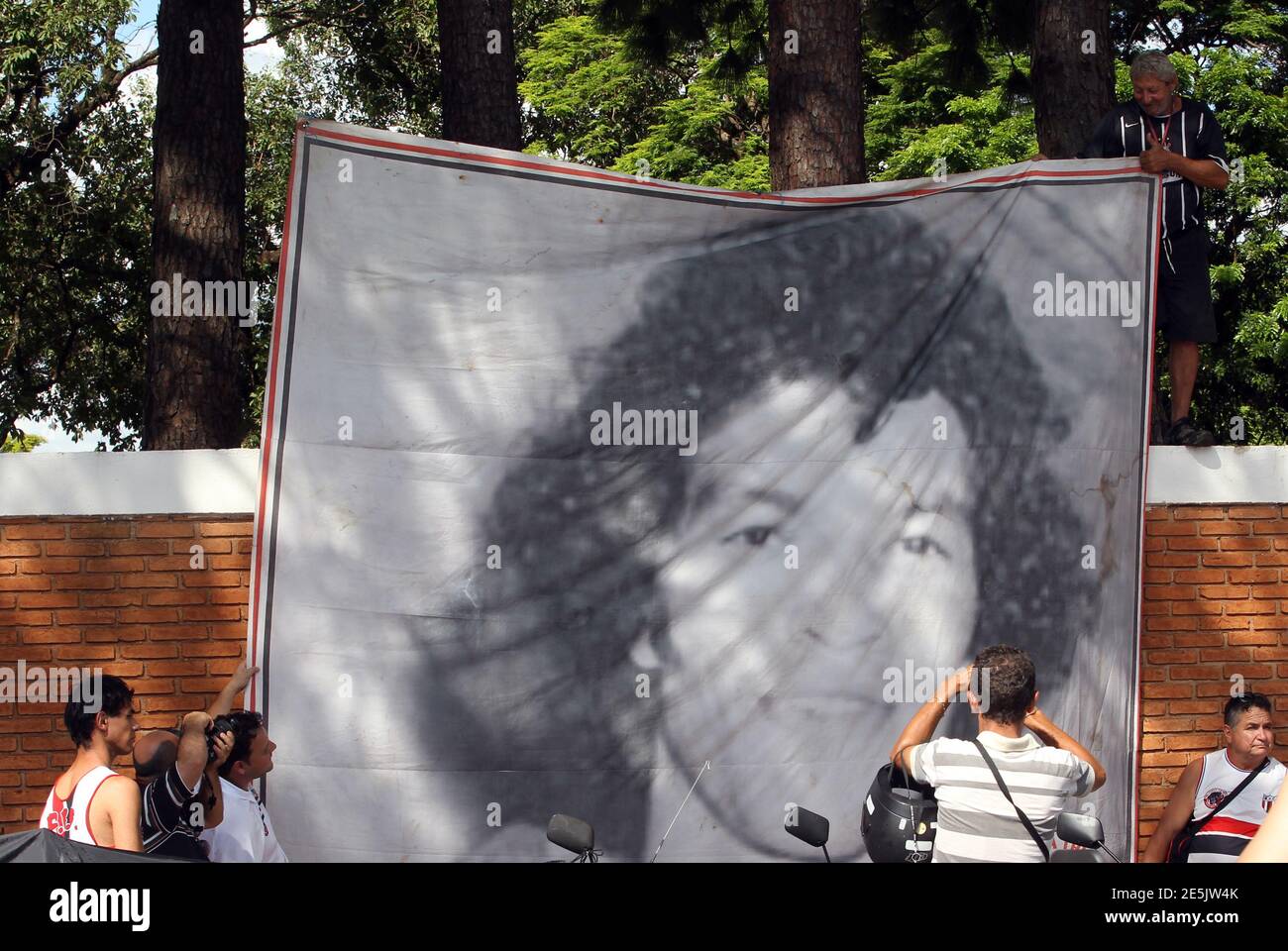 People display a flag with an image of Brazil's 1982 World Cup captain Socrates before his funeral ceremony, in front of the cemetery in Ribeirao Preto December 4, 2011. Socrates, the 'Golden Heel' renowned as one of the great playmakers of his generation, died in hospital on Sunday of septic shock at the age of 57, his doctors said in a statement. REUTERS/Paulo Whitaker (BRAZIL - Tags: SPORT SOCCER OBITUARY) Stock Photo
