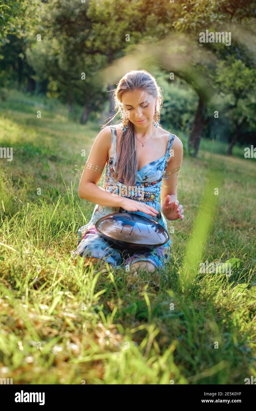 Beautiful hipster woman sitting in the park and playing on happy drum and singing Stock Photo