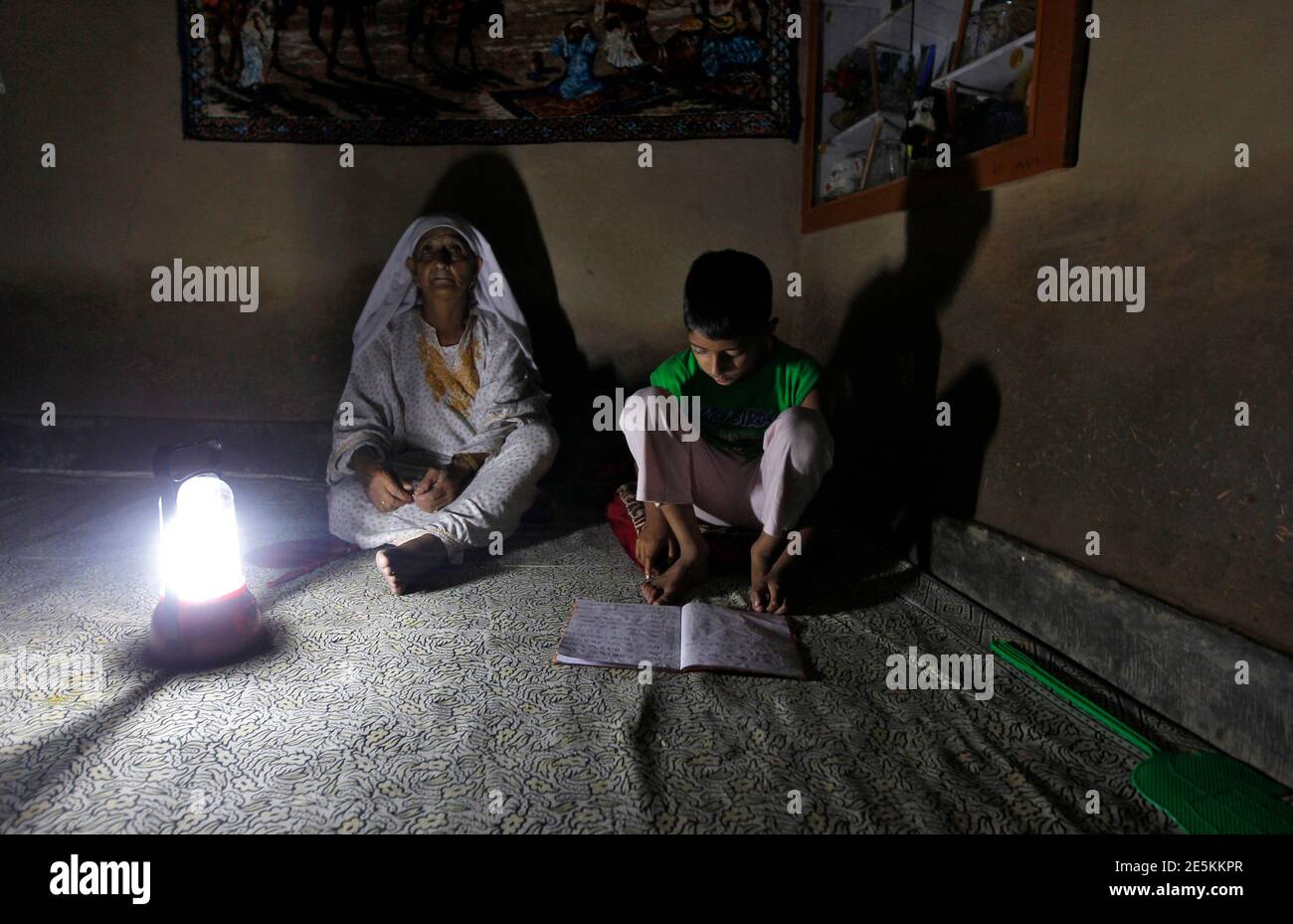 A Kashmiri boy reads a book while sitting next to his grandmother during a power-cut due to curtailment, at their house in Srinagar July 3, 2013. India is betting a gas price hike will boost supply and help fix the country's chronic power shortages, but the plan may falter unless the debt-laden industry can pass on higher energy costs to consumers or win government subsidies. Picture taken July 3, 2013. To match INDIA-POWER/ REUTERS/Danish Ismail (INDIAN-ADMINISTERD KASHMIR - Tags: POLITICS BUSINESS INDUSTRIAL ENERGY) Stock Photo