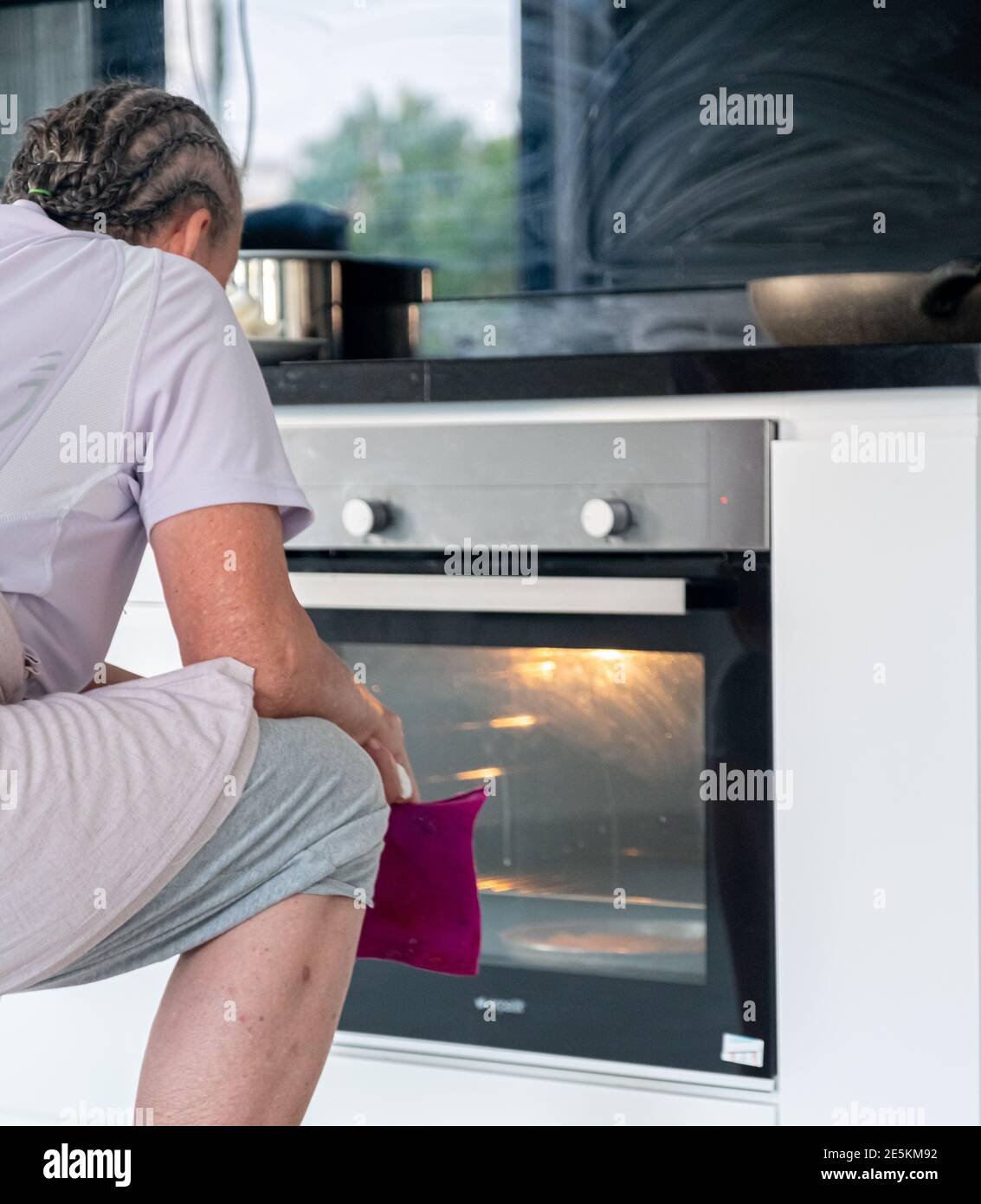 Granny is waiting front of the electric oven to finish cooking in Stock