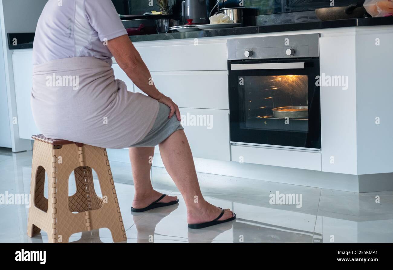 Granny is waiting front of the electric oven to finish cooking in Stock