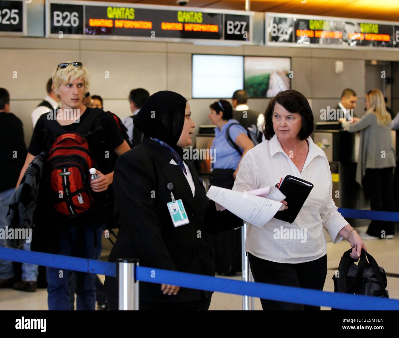A Qantas Airways employee walks ticket holders over to the Singapore Airlines ticket counter, as she works to rebook them on a different flight, at Los Angeles International Airport (LAX) October 29, 2011. Tens of thousands of stranded Qantas Airways passengers are pinning their hopes on a government-appointed tribunal on Sunday ordering an end to the industrial action that grounded the Australian national carrier's entire fleet.  REUTERS/Danny Moloshok (UNITED STATES - Tags: TRANSPORT BUSINESS EMPLOYMENT) Stock Photo