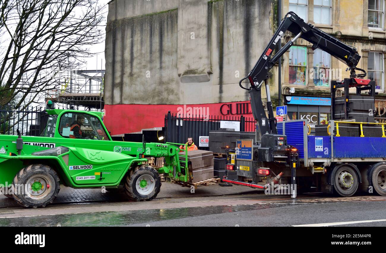 Construction site with concrete blocks being delivered from vehicle with crane at back stopped on road, forklift wtih telescopic arm collecting. Very Stock Photo