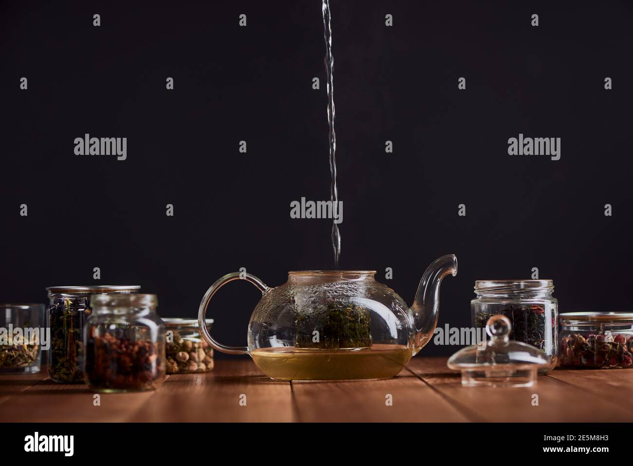 Boiling water pouring into a glass pot with green tea leaves Stock