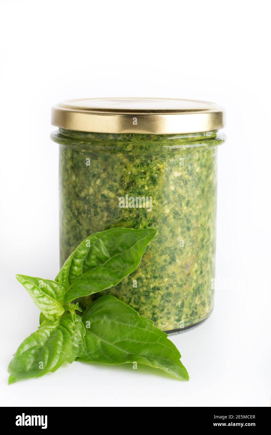 Pesto sauce in a glass jar isolated with fresh basil leaves on white