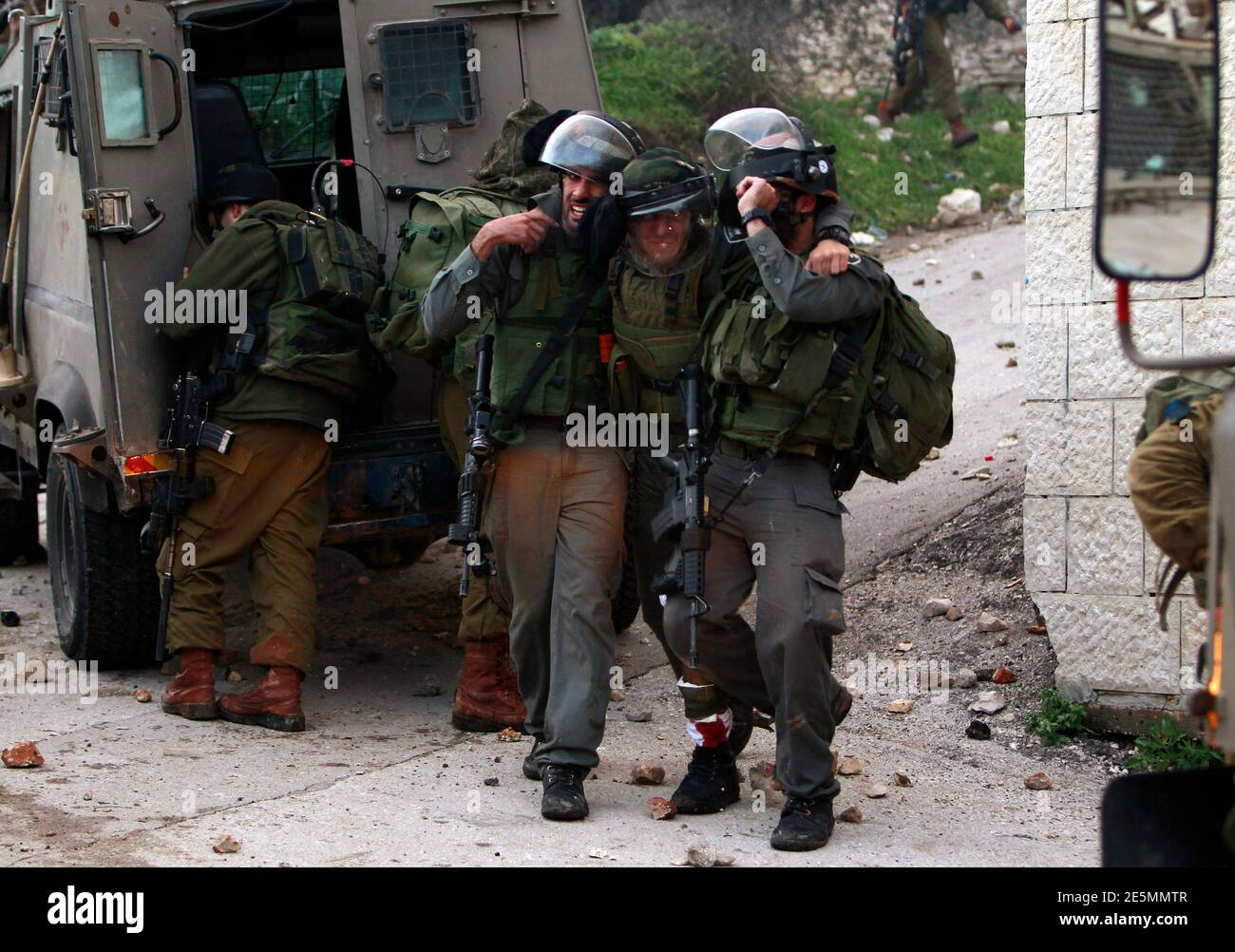 Israeli border police officers help an injured officer during clashes with stone throwing Palestinians protesting against a nearby Jewish settlement in the West Bank village of Burin, south of Nablus February 2, 2013. Israeli soldiers used tear gas and stun grenades on Saturday to disperse about 150 Palestinians trying to block expansion of Israeli settlements in the occupied West Bank.  Both sides sustained light injuries as the soldiers removed about a dozen tents and small huts from land adjacent to the Palestinian northern West Bank village of Burin, Palestinian witnesses and the Army said Stock Photo