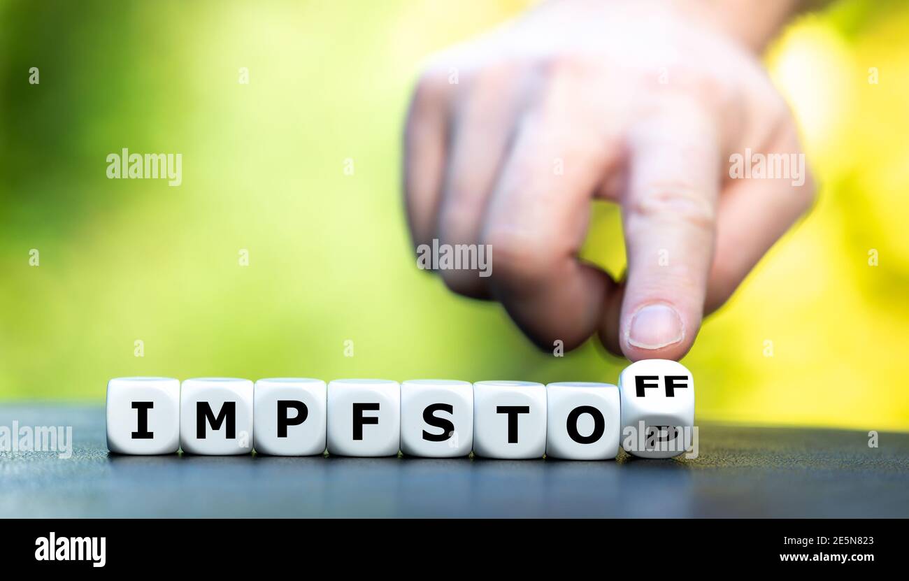 Hand turns dice and changes the German word 'Impfstop' (vaccination stop) to 'Impfstoff' (vaccine). Stock Photo
