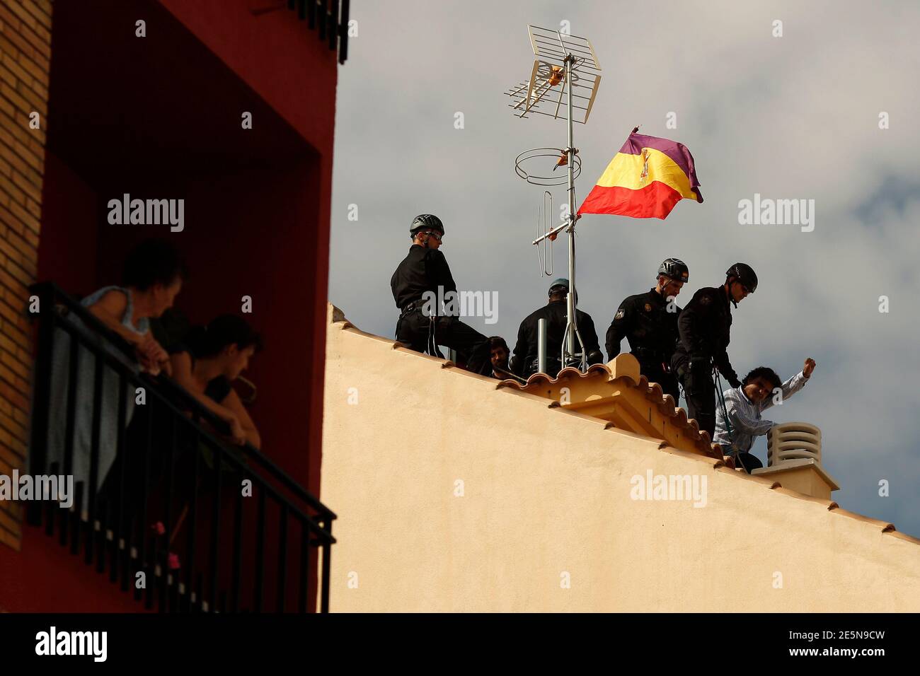 An activist raises his fist as he is detained by police next to a Spanish Republican era flag on a roof after Spanish riot police evicted several families of an unoccupied building of flats in Malaga, southern Spain October 3, 2013. A total of 13 families, included 12 children, had occupied the building since February. Members from various support platforms failed to stop the eviction and three activists were arrested when they refused to leave the roof of building, according to local media. REUTERS/Jon Nazca (SPAIN - Tags: CIVIL UNREST POLITICS BUSINESS REAL ESTATE SOCIETY) Stock Photo