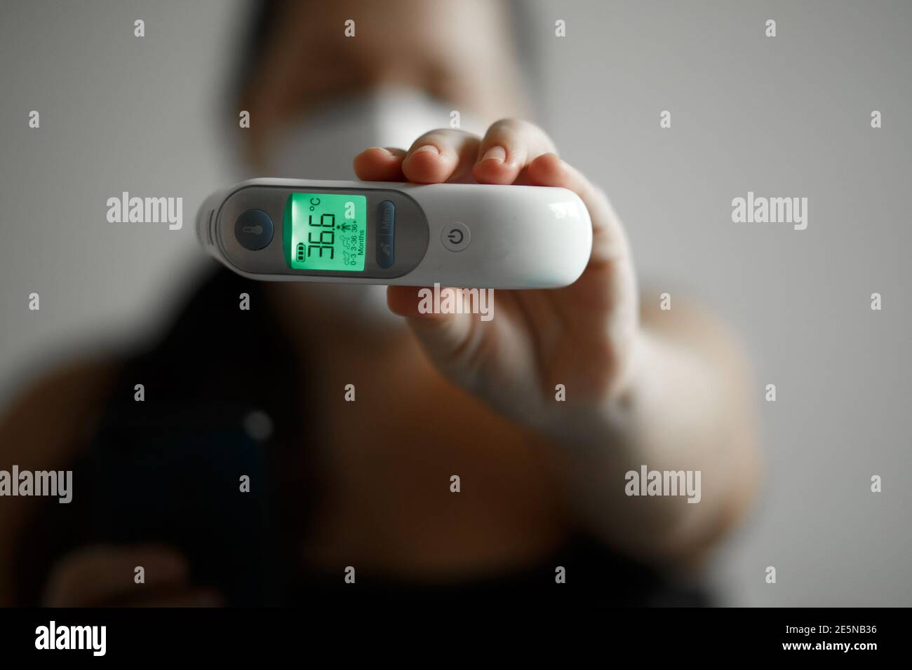 Girl in a mask on a white background holding a thermometer, medical theme Stock Photo