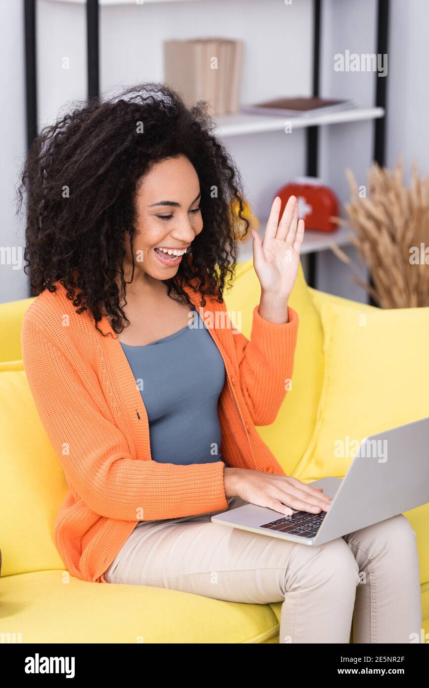 happy african american woman waving hand during video call at home ...