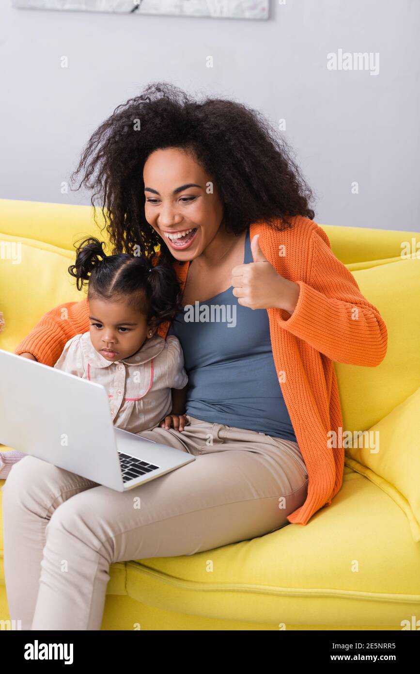 happy african american mother showing thumb up during video call near toddler daughter Stock Photo