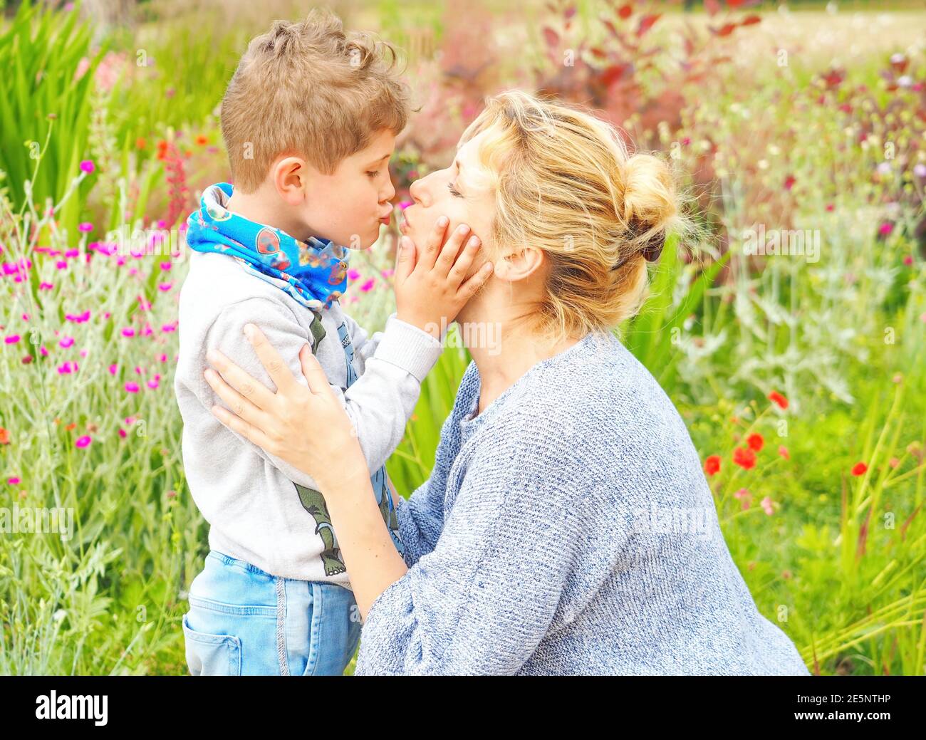 Mother and son hug and kiss in the garden with flowers Stock Photo