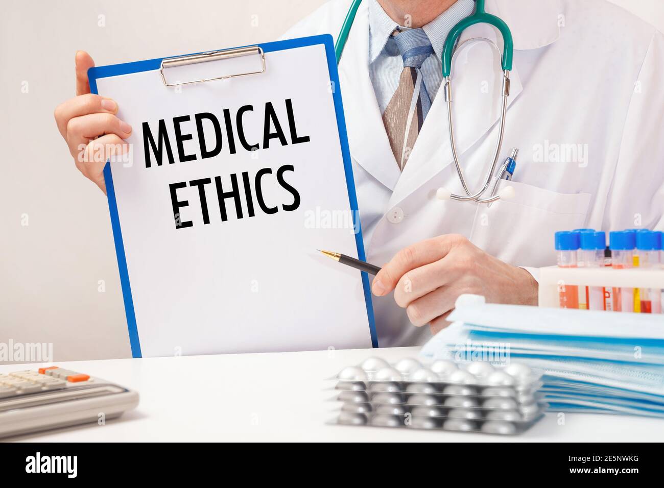 Doctor holds paper with inscription Medical Ethics, stethoscope and pills on table Stock Photo