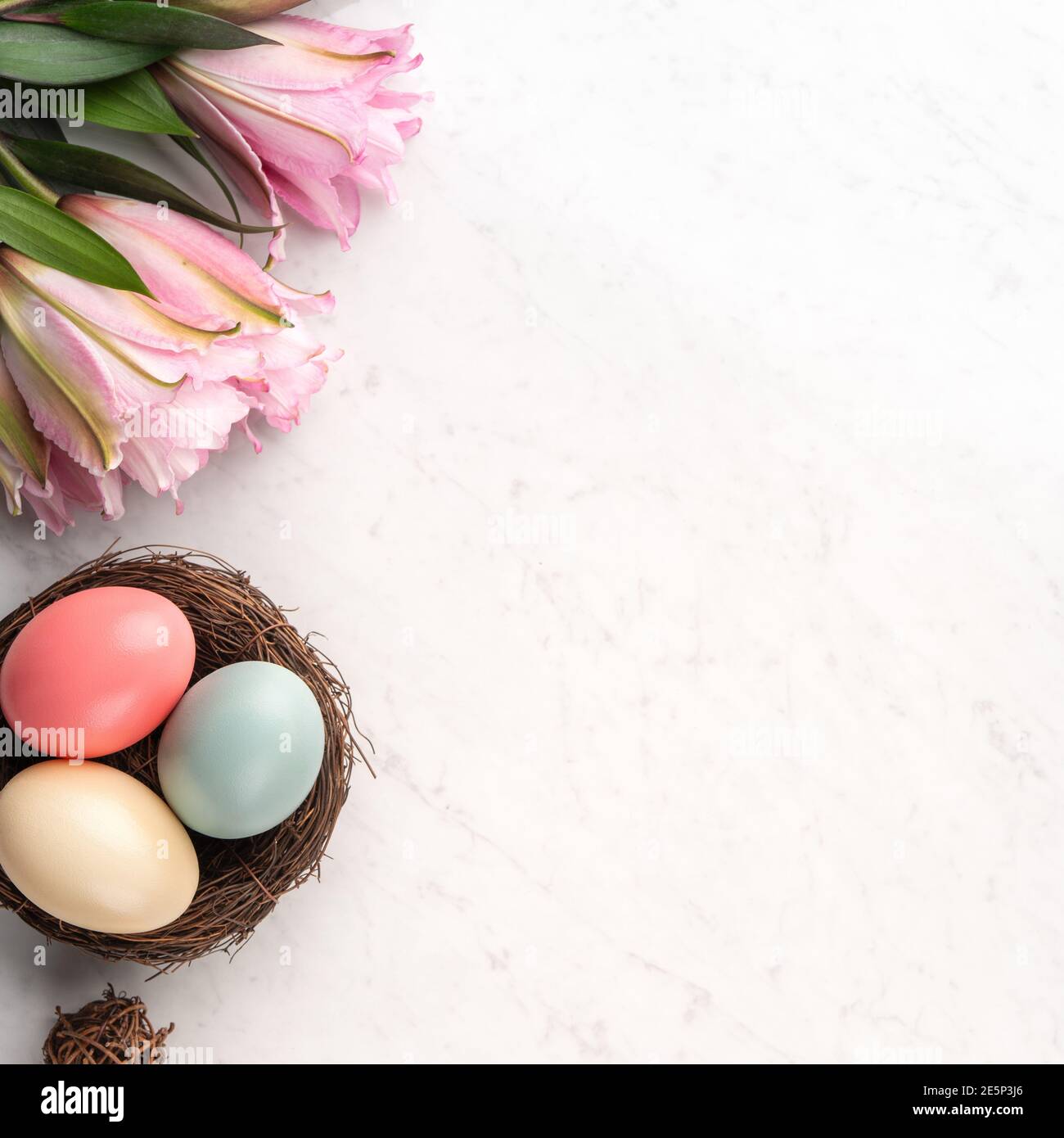 Colorful Easter eggs in the nest with pink lily flower on bright marble ...