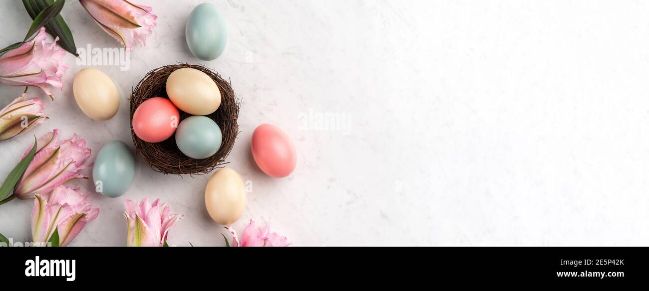 Colorful Easter eggs in the nest with pink lily flower on bright marble ...