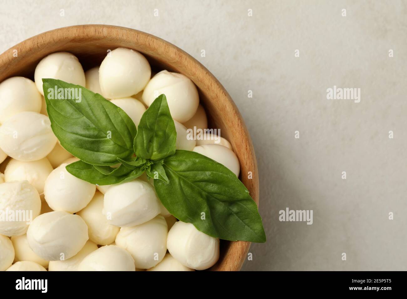 Bowl with mozzarella and basil on white textured background, space for text Stock Photo